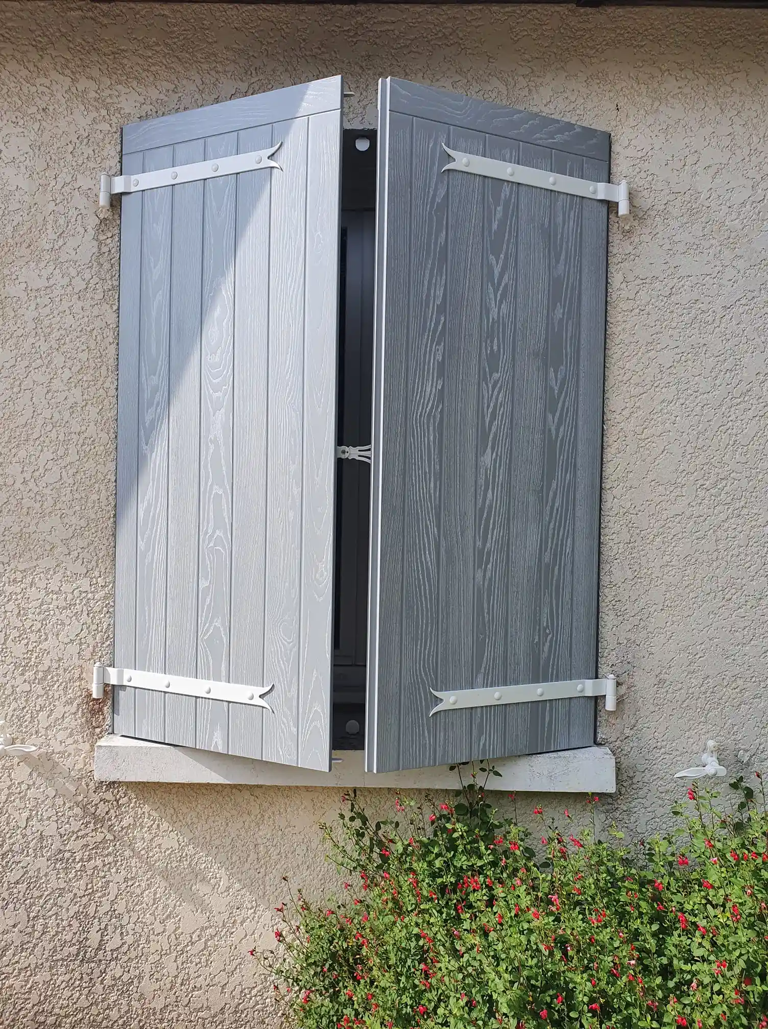Volets battants composites ISOCOULEURS veinés gris, à aspect emboîture haute et pentures blanches, posés sur une façade