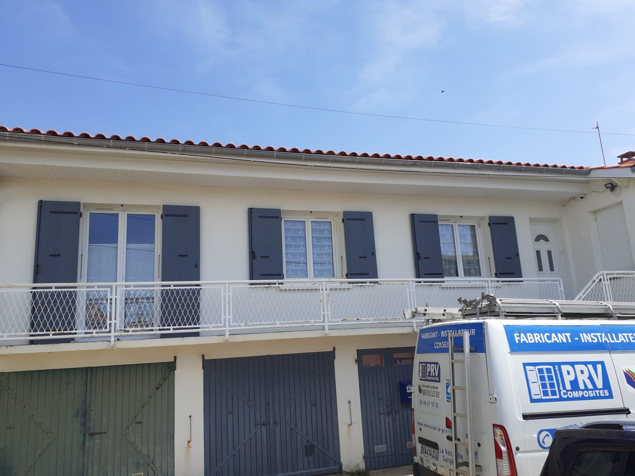 Maison à étage avec des volets battants composites gris foncé posés aux fenêtres, une camionnette PRV Composites garée devant