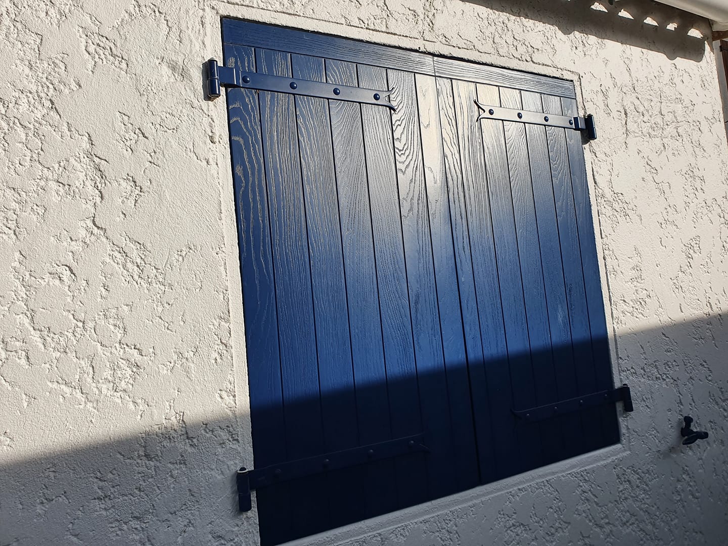 Volets battants composites bleus à aspect emboîture haute, fermés sur une façade crépie