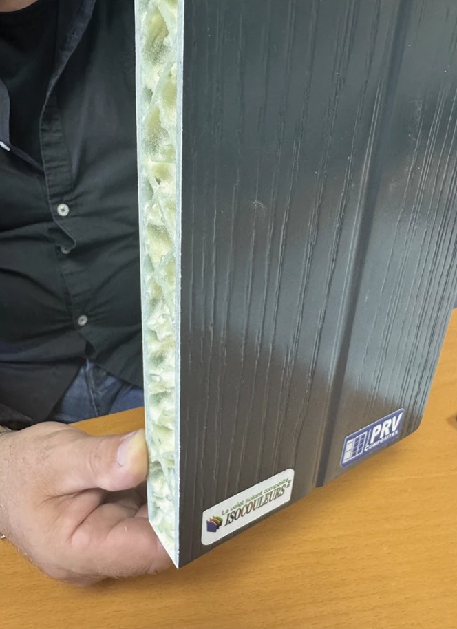 Panneau composite ISOCOULEURS® veiné gris tenu à la main et vu en tranche : l'âme isolante apparaît entre les deux parois