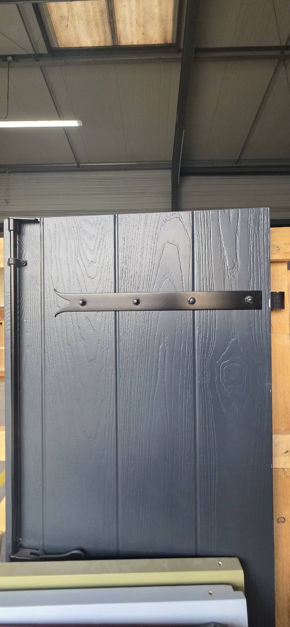 Gros plan sur un vantail composite veiné bleu foncé avec penture noire et espagnolette, en atelier